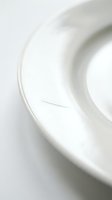 Close-up of white ceramic plate with smooth curved edges and subtle shadows on neutral background for minimalist kitchen and dining concepts.