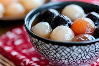 Traditional Asian dessert with colorful glutinous rice balls in sweet soup served in decorative black bowl on red checkered cloth, close up view of authentic cuisine.
