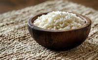 Cooked white rice in rustic wooden bowl on textured natural fiber mat, perfect for food blogs and culinary content.