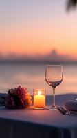 Romantic dinner table setting with wine glass, candle and flowers at sunset by water for anniversary celebration or date night dining experience.