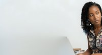 Young Black woman with braided hair and silver hoop earrings working on laptop, wearing patterned shirt, isolated on white background for business and technology design projects.