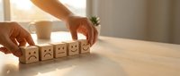 Hand selecting happy face wooden block from row of emotion cubes on desk. Customer satisfaction feedback rating concept for business evaluation.