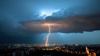 Dramatic lightning strike illuminates night cityscape as storm clouds hover above urban landscape, creating spectacular natural light show over metropolitan area.