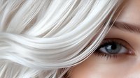Close up view of bright blue eye with platinum blonde wavy hair strands flowing across face, showcasing natural beauty and modern hairstyling trends.