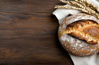 Freshly baked artisanal sourdough bread dusted with flour on white cloth against dark wooden background with golden wheat stalks, copy space.