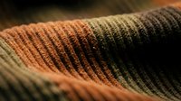 Close-up macro shot of colorful knitted wool fabric texture showing detailed stitching patterns in warm orange and dark green tones for textile design.