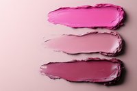 Pink and mauve lipstick smears showing texture and different shades on light pink background, cosmetic product swatches demonstrating color variety and consistency.