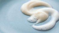 White cream cosmetic swirls on light blue background for skincare and beauty product advertising campaigns.