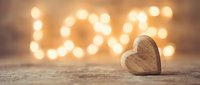 Wooden heart on rustic surface with glowing bokeh lights forming the word LOVE in warm golden tones, romantic Valentine's Day concept.