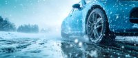 Blue car with winter tire on snowy road during snowfall, close-up view of wheel on wet icy asphalt in cold weather conditions.