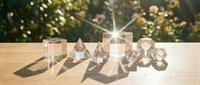 Crystal clear geometric shapes arranged on wooden surface in sunlight, casting rainbow light refractions with blurred garden background.