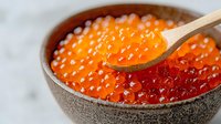Fresh red and orange salmon caviar in ceramic bowl with wooden spoon on marble background, close up view of luxury seafood delicacy.