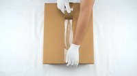 Worker in white cotton gloves sealing cardboard box with tape for shipping and delivery logistics operations.
