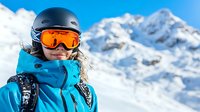 Young female skier in bright blue winter jacket and protective gear against snowy mountain backdrop, enjoying winter sports activities in alpine setting.