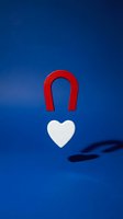 Red horseshoe magnet attracting white heart shape on blue background symbolizing love attraction and romantic magnetism for relationship concepts.