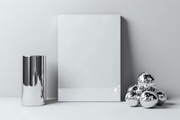 Minimalist mockup composition with blank white canvas, metallic silver vase, and decorative chrome spheres on white surface against gray background.