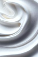 Smooth swirling texture of white cream or foam creating soft waves and curves, macro photography with shallow depth of field for cosmetic and food industry use.