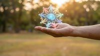 Hand holding glowing geometric crystal star shape with magical light effects in natural outdoor setting during golden hour sunset.