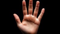 Open palm of light-skinned hand against dark background showing five fingers spread wide, dramatic side lighting creates shadows and depth for conceptual use.
