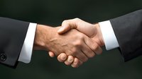 Professional business handshake between two people wearing formal suits against dark green background symbolizing partnership agreement and successful deal closing.