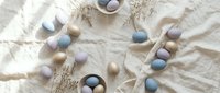 Pastel Easter eggs in neutral tones scattered on white linen fabric with decorative nests for spring holiday celebration and seasonal decoration.