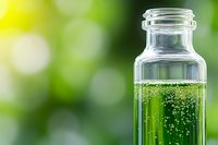 Clear glass bottle with green liquid and bubbles against blurred natural background for wellness, aromatherapy, and organic skincare concepts.