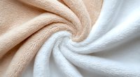 Soft twisted fabric texture in beige and white colors creates elegant swirl pattern, macro close up view of plush microfiber or fleece material background.