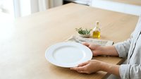 Person with empty plate and olive oil bottle on wooden table, representing healthy eating, diet concept, or food preparation in modern kitchen setting.