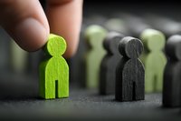 Fingers selecting green wooden figure from group of black and green people silhouettes, symbolizing recruitment, talent acquisition, and team building.
