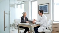 Professional doctor consulting with mature businesswoman patient in modern medical office discussing health results and treatment options.