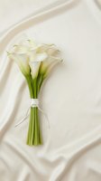 Elegant white calla lily bouquet tied with ribbon on soft cream silk fabric for wedding ceremonies and romantic celebrations.