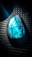 Polished labradorite gemstone displaying brilliant blue flash and iridescent colors on dark woven textile background for luxury jewelry and mineral collection designs.