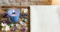 Spa wellness setup with burning candle, lavender, crystals and flowers on wooden tray for relaxation and aromatherapy meditation sessions.