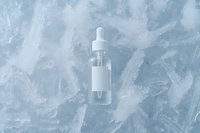 Clear glass dropper bottle with blank white label on frosty ice crystal background, minimalist winter skincare concept for cosmetic and beauty product photography.