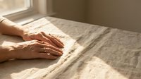 Woman hands touching soft linen fabric texture in warm sunlight. Natural home textile material for interior design and comfort living concepts.