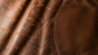 Rich brown leather texture with natural grain patterns and soft folds creating luxurious material surface for fashion and interior design applications.