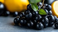 Fresh dark purple grapes with water drops and green leaves on gray background, selective focus with blurred yellow lemons, macro food photography.