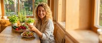 Happy middle-aged Caucasian woman enjoying healthy meal with fresh vegetables and herbs in bright modern kitchen for wellness lifestyle content.
