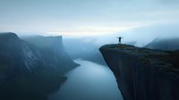 Silhouette of person with raised arms standing on cliff edge overlooking dramatic fjord landscape in moody blue atmospheric morning light with misty mountains.