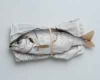 Fresh whole sea bass wrapped in newspaper tied with string, isolated on white background, top view seafood concept.
