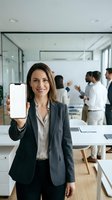 Professional businesswoman displaying blank smartphone screen in modern office with colleagues working in background for mobile app presentation.