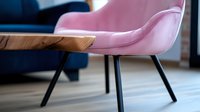 Modern pink velvet armchair with black metal legs next to wooden table edge against blue sofa in contemporary living room interior with soft focus effect.