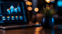 Modern workspace with laptop displaying financial charts and decorative plant in evening office setting with warm bokeh lighting effects.
