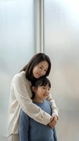 Asian mother embracing young daughter in modern home interior showing family love and bonding moment together in casual comfortable clothing.