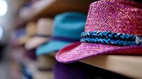 Pink straw fedora hat with blue braided band displayed on retail shelf among other summer hats, shallow depth of field creates soft background blur.