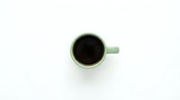 Green ceramic coffee mug with black coffee viewed from above on white background, isolated for design use in cafes and morning beverage concepts.