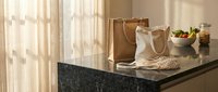 Modern kitchen counter with grocery bags and fresh produce in warm natural sunlight streaming through window curtains creating cozy domestic atmosphere.