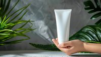 White cosmetic tube floating above female hand with tropical leaves and misty atmosphere. Minimalist skincare product presentation on light background.