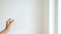 Hand reaching toward blank white wall with natural light from window, suitable for concepts of aspiration, reaching goals, minimalist design, and empty space messaging.