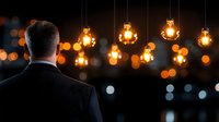 Businessman in dark suit looking at glowing vintage Edison bulbs hanging against blurred city lights background, creating atmospheric business ambiance.